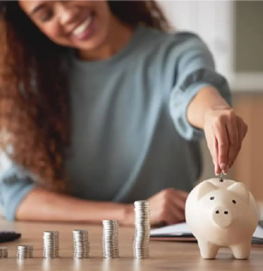 Persona sonriendo mientras guarda monedas en una alcancía, simbolizando el ahorro y la gestión financiera