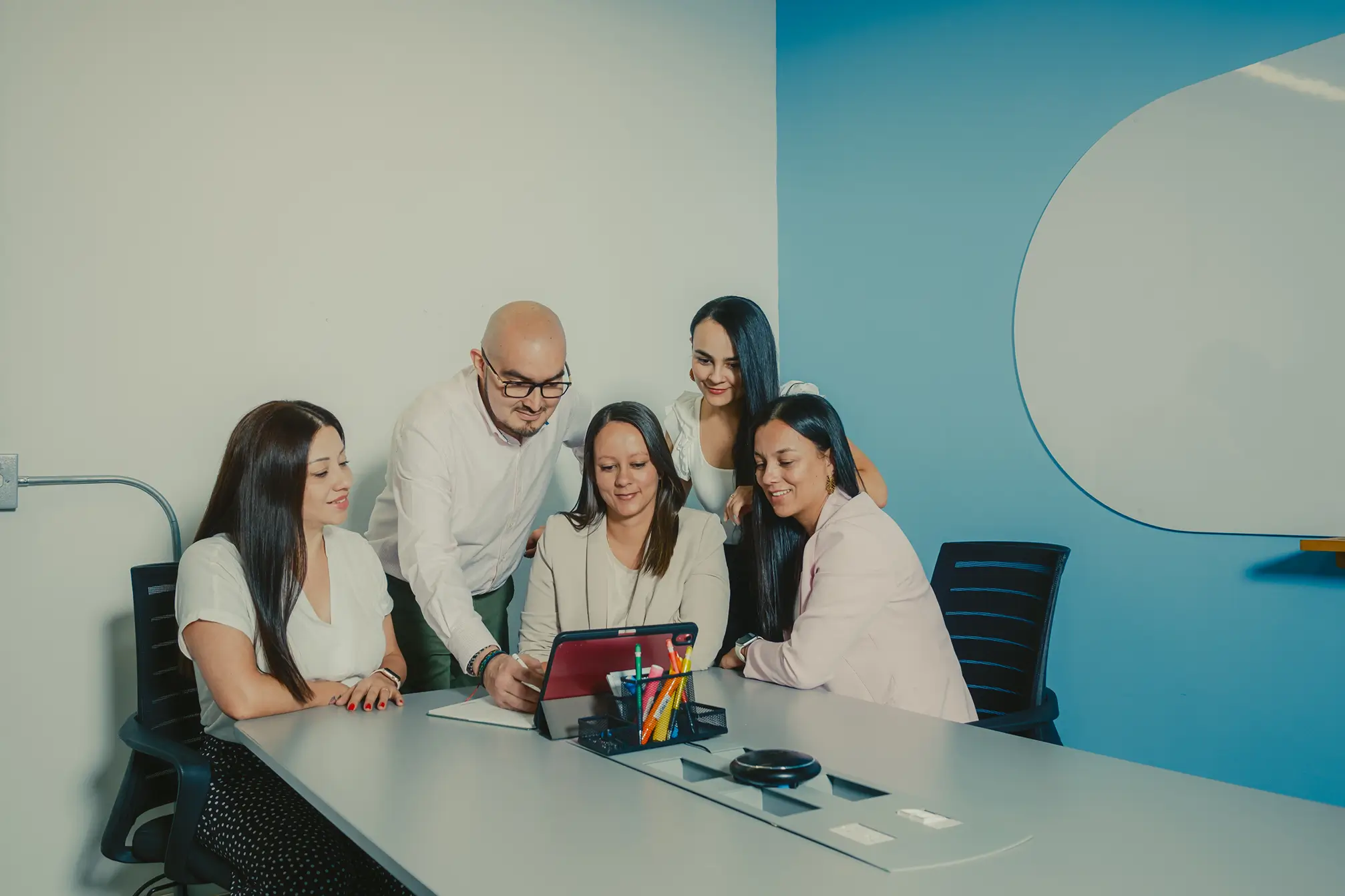 Un grupo de cinco personas en una reunión de trabajo, observando una tablet y colaborando en un proyecto, en un ambiente de oficina moderno y profesional